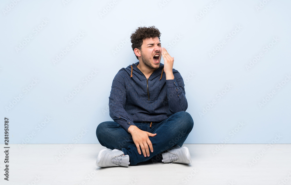 Young man sitting on the floor yawning and covering wide open mouth with hand Young man sitting on the floor yawning and covering wide open mouth with hand
