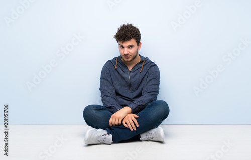 Young man sitting on the floor with sad and depressed expression © luismolinero