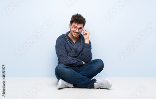 Young man sitting on the floor with glasses and happy © luismolinero