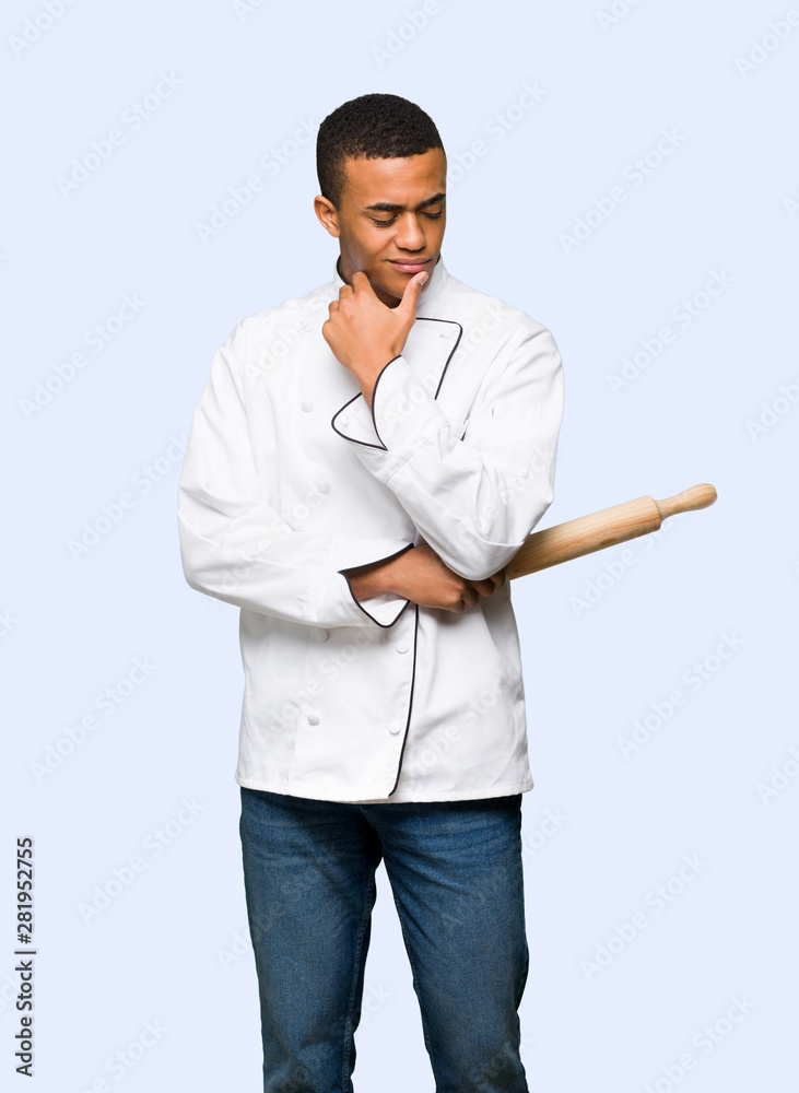 Young afro american chef man looking down with the hand on the chin on isolated background Young afro american chef man looking down with the hand on the chin on isolated background