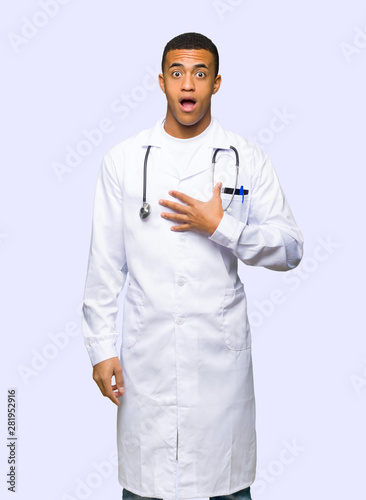 Young afro american man doctor surprised and shocked while looking right on isolated background