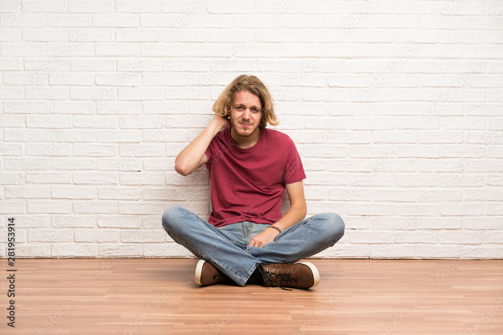 Blonde man sitting on the floor having doubts
