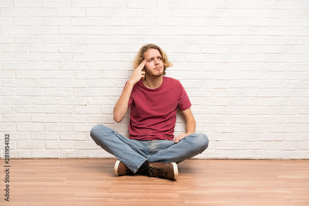 Blonde man sitting on the floor with problems making suicide gesture Blonde man sitting on the floor with problems making suicide gesture