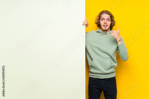 Blonde man holding a big empty placard making phone gesture