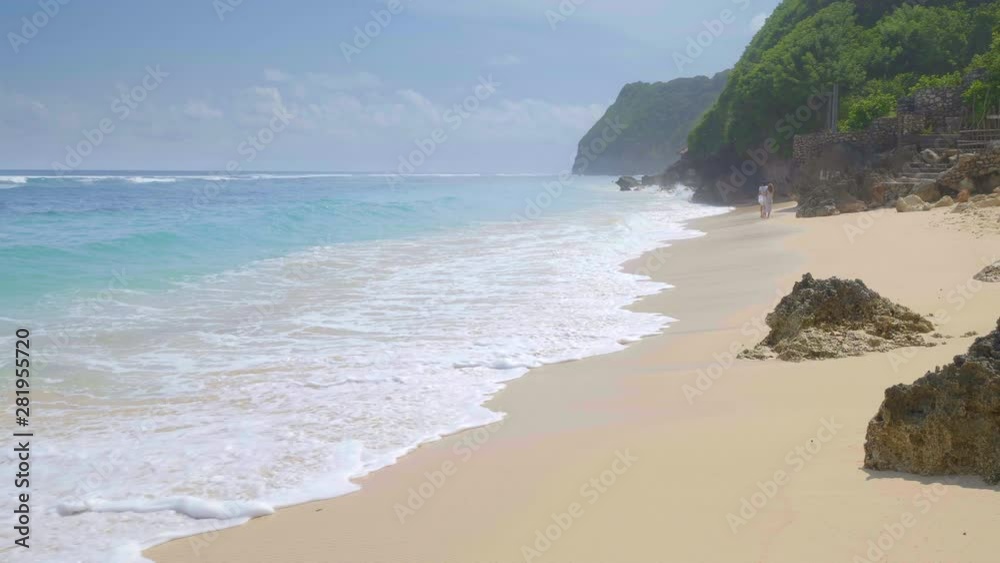 A couple is walking in tropical beach with big waves and fog near huge rocks filmed in slow motion A couple is walking in tropical beach with big waves and fog near huge rocks filmed in slow motion