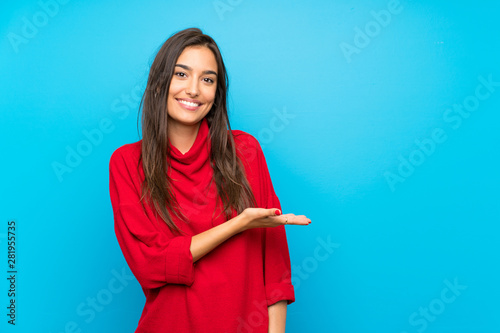 Young woman with red sweater over isolated blue background extending hands to the side for inviting to come