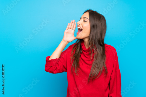 Young woman with red sweater over isolated blue background shouting with mouth wide open photo