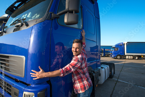 Happy caucasian truck driver loving his job. Trucker hugging his truck vehicle for transportation.