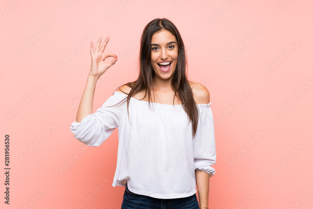 Young woman over isolated pink background surprised and showing ok sign Young woman over isolated pink background surprised and showing ok sign