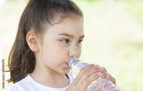 Cute adorable child girl drinking clear water outdoors.