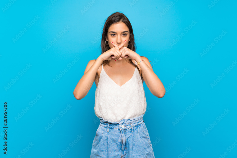 Young woman over isolated blue background showing a sign of silence gesture Young woman over isolated blue background showing a sign of silence gesture