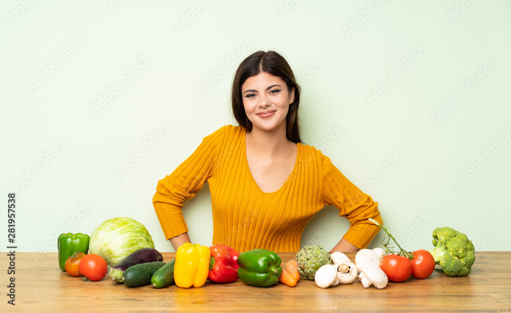 Fototapeta premium Teenager girl with many vegetables posing with arms at hip and smiling
