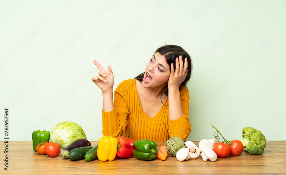 Teenager girl with many vegetables surprised and pointing finger to the side Teenager girl with many vegetables surprised and pointing finger to the side