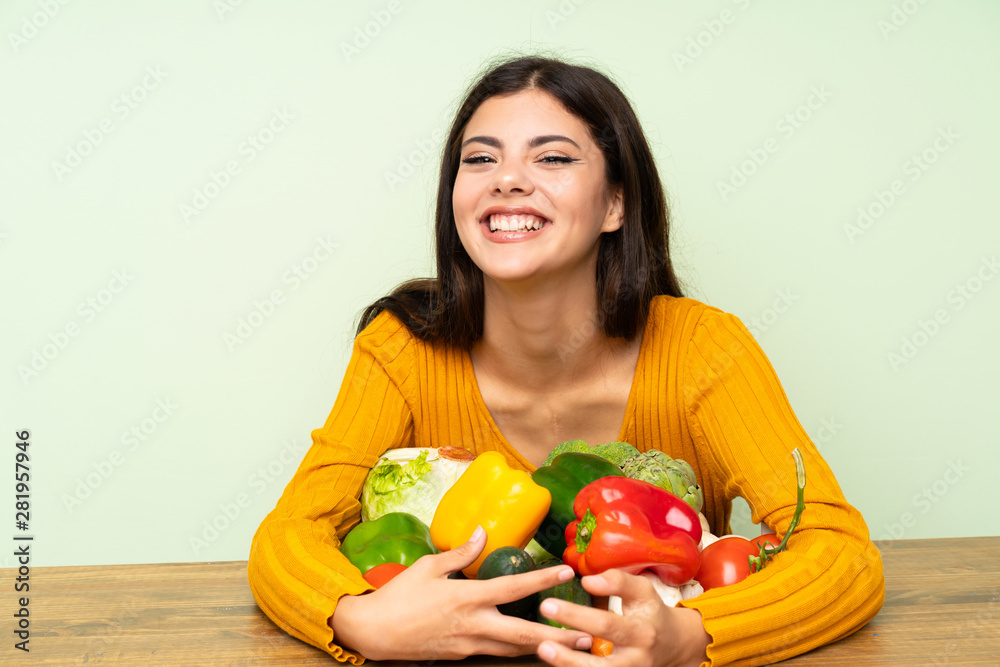 Fototapeta premium Happy Teenager girl with many vegetables over green wall