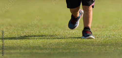 Running children detail on sport shoes running along green grass