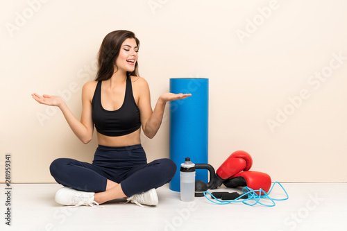 Fototapeta Naklejka Na Ścianę i Meble -  Teenager sport girl sitting on the floor holding copyspace with two hands