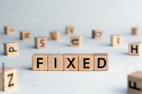 Fixed - word from wooden blocks with letters, fixed interest rates or costs  concept, random letters around, top view on wooden background