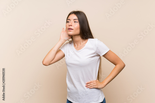 Pretty young girl over isolated background listening to something by putting hand on the ear
