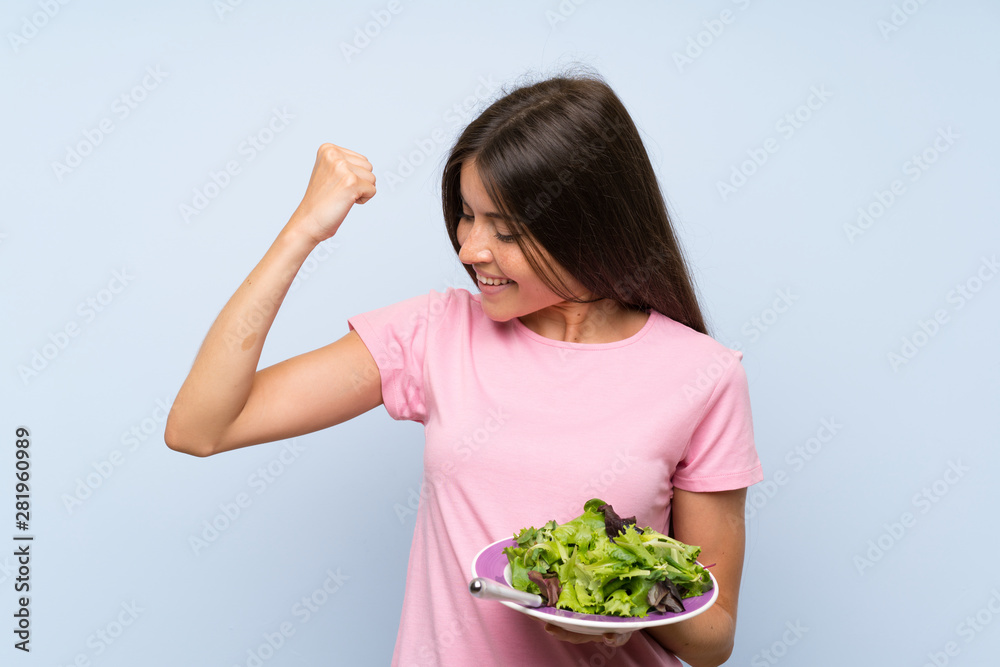 Young woman with salad over isolated blue background celebrating a victory Young woman with salad over isolated blue background celebrating a victory