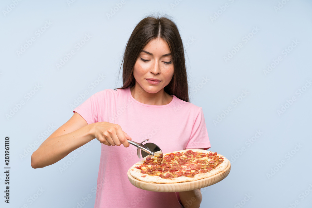 Pretty young girl holding a pizza over isolated blue wall Pretty young girl holding a pizza over isolated blue wall