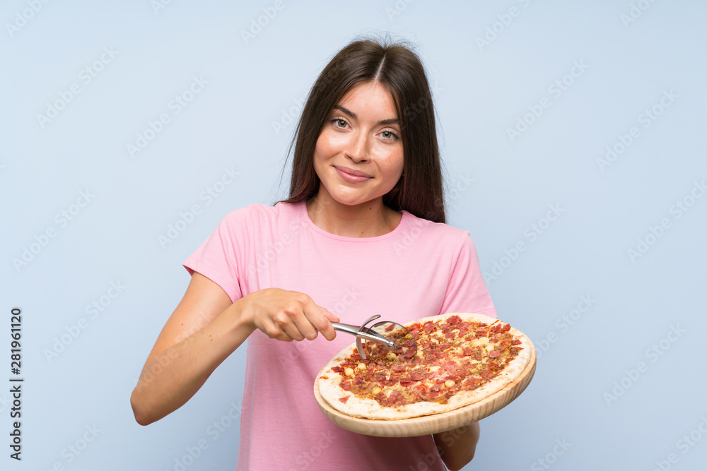 Pretty young girl holding a pizza over isolated blue wall