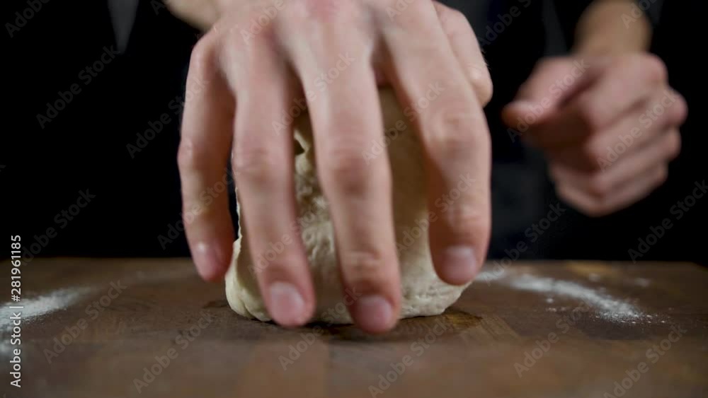 Cook rolls out dough on a wooden table in a dark kitchen Cook rolls out dough on a wooden table in a dark kitchen