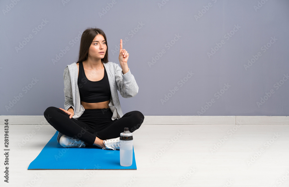 Young sport woman sitting on the floor with mat touching on transparent screen Young sport woman sitting on the floor with mat touching on transparent screen