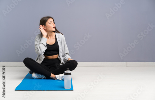 Young sport woman sitting on the floor with mat listening something