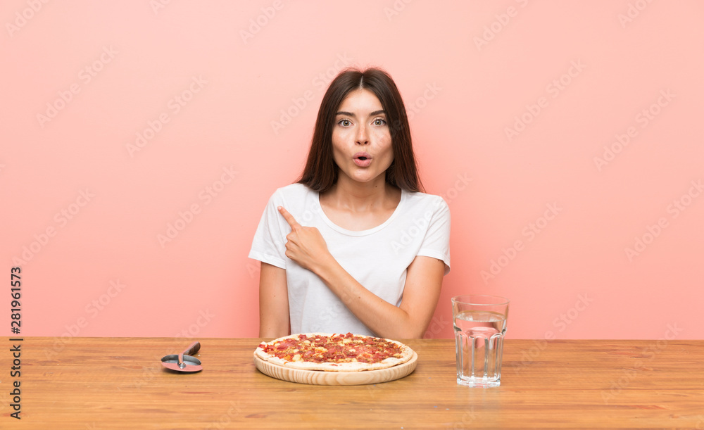 Young woman with a pizza surprised and pointing side Young woman with a pizza surprised and pointing side
