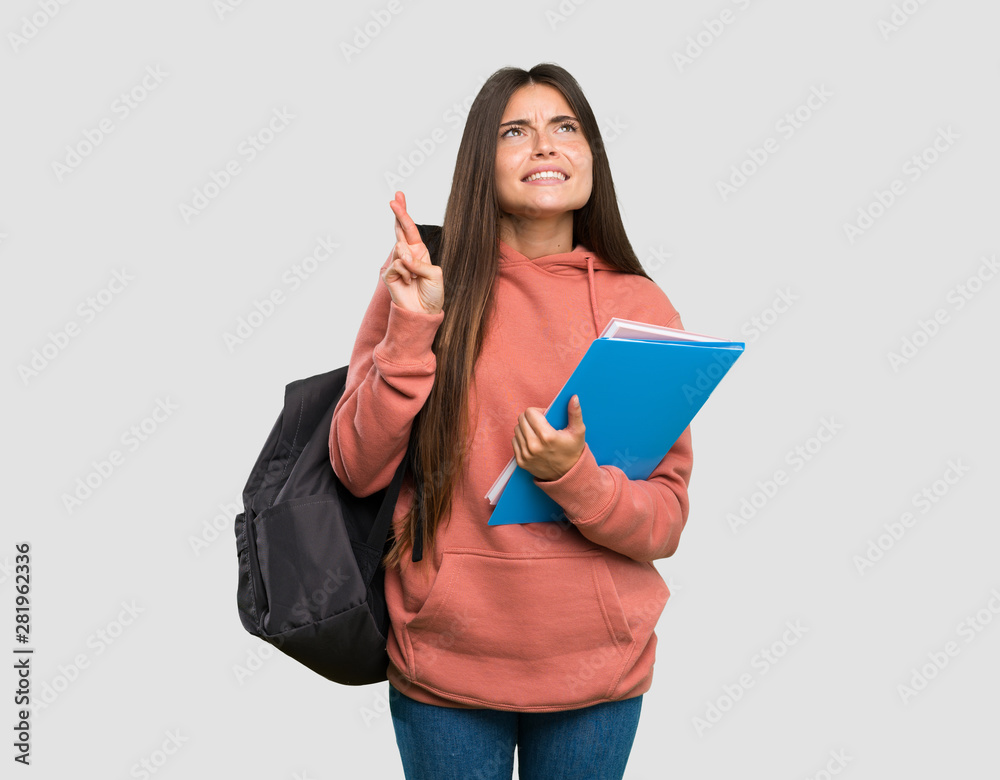 Young student woman holding notebooks with fingers crossing and wishing the best over isolated grey background Young student woman holding notebooks with fingers crossing and wishing the best over isolated grey background