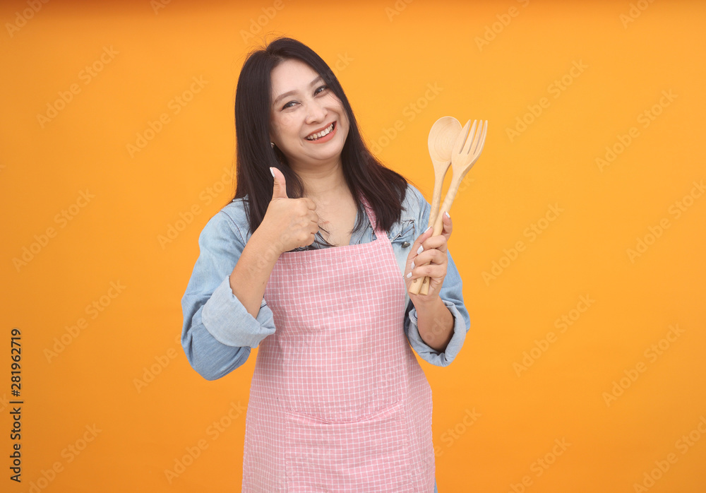 Happy Asian woman is cooking with apron for cooking advertise theme on on yellow background. Happy Asian woman is cooking with apron for cooking advertise theme on on yellow background.