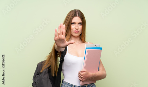 Young student woman over isolated green background making stop gesture with her hand