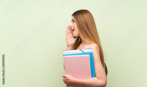 Young student woman over isolated green background shouting with mouth wide open
