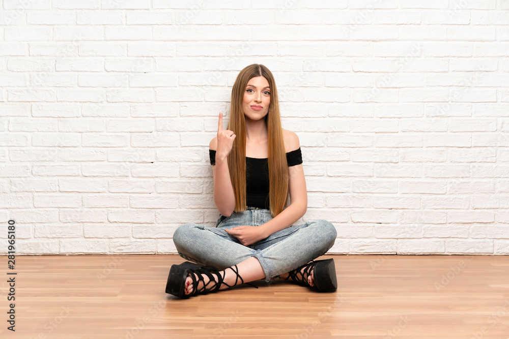 Young woman sitting on the floor pointing with the index finger a great idea