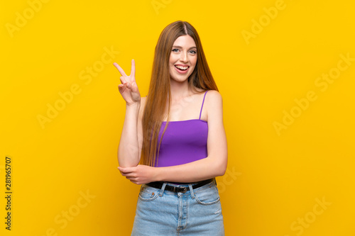 Young woman over isolated yellow background smiling and showing victory sign