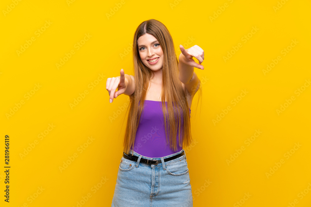 Young woman over isolated yellow background points finger at you while smiling Young woman over isolated yellow background points finger at you while smiling