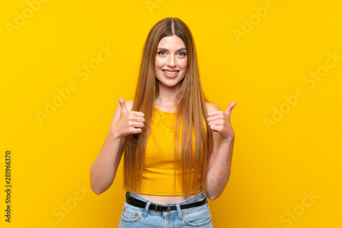 Young woman over isolated yellow background giving a thumbs up gesture