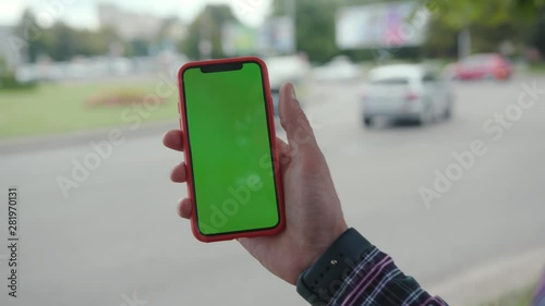 Male hand showing green screen chromekey mobile phone in the street background. Young businessman using a smartphone outdoors in busy city center. photo