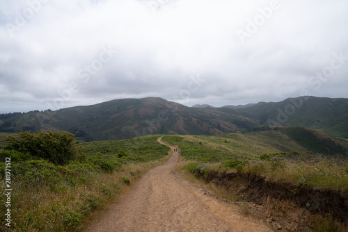 Long, winding hiking trail leading to mountains with two hikers marching into distance