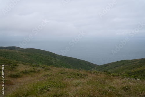 Green hills, hiking path leading to the Pacific ocean on overcast day