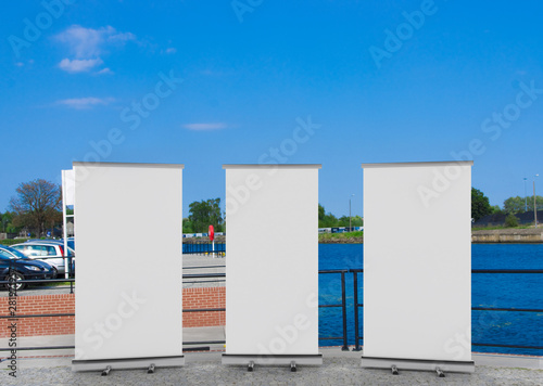 3D rendering of blank vertical rollup (empty billboard advertisement) with city background. Empty mockup template