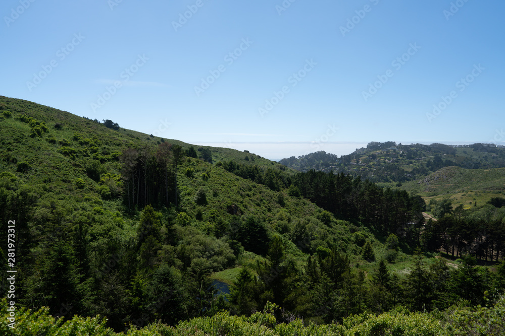 Scenic green hills, trees, grass, blue clear skies, residential housing in distance