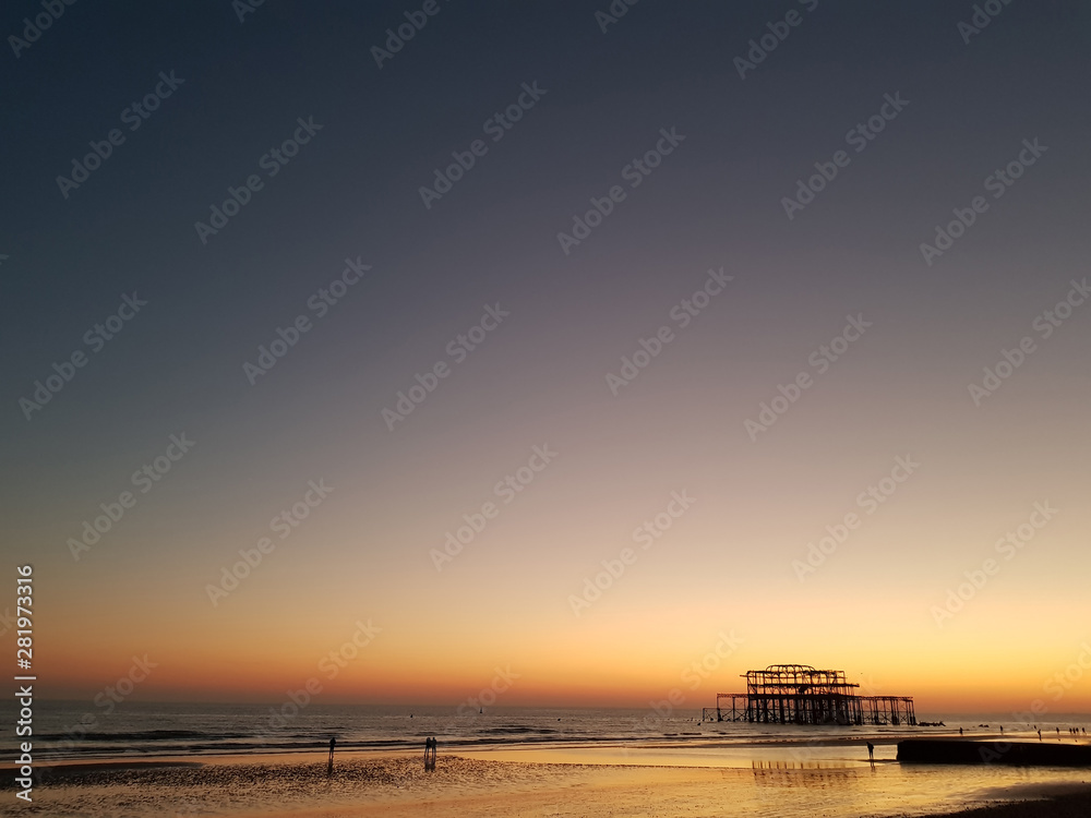 Beautiful sunset view at Brighton Pier with Brighton beach sea, sand and the oldest building in the background. Popular landmark of the city.