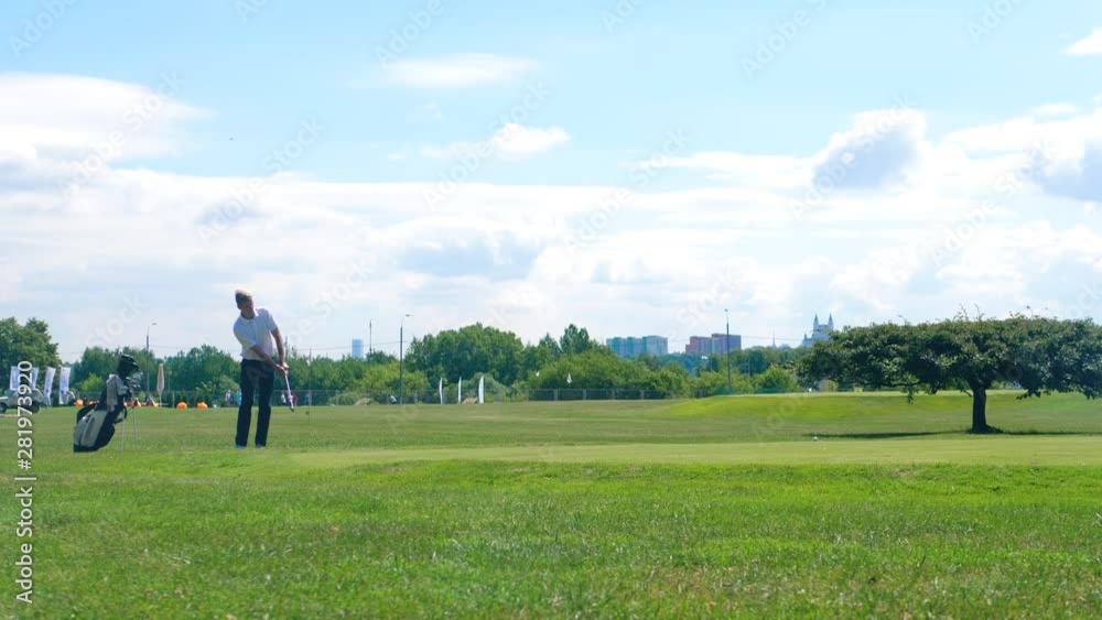 A man hits a small ball while playing golf on a field. Golf player on a golf course. A man hits a small ball while playing golf on a field. Golf player on a golf course.