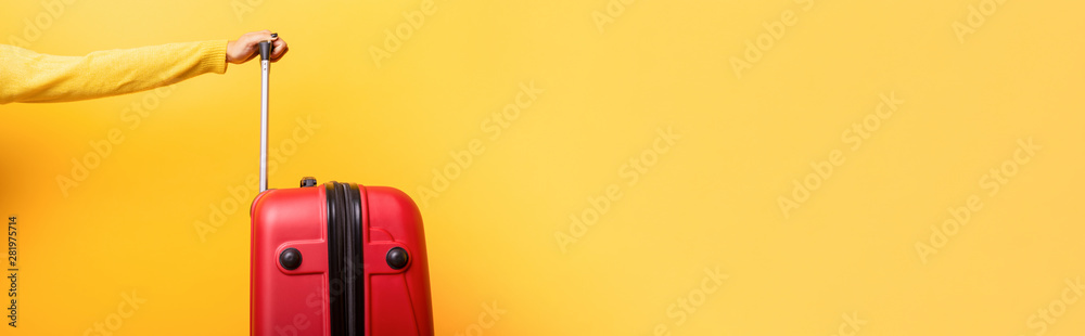 Fototapeta premium Travel red suitcase and hand over yellow background, panoramic mock up image