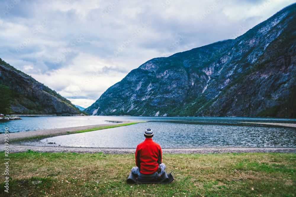 man making yoga meditation on mats in cloudy morning outdoors near beautiful lake Norway. Yoga meditation in mountains man traveler relaxing alone. Lotus pose. vacations outdoor harmony with nature