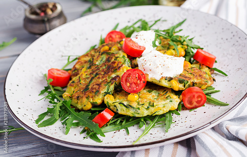 Zucchini pancakes with corn and sour cream served arugula, tomatoes salad.