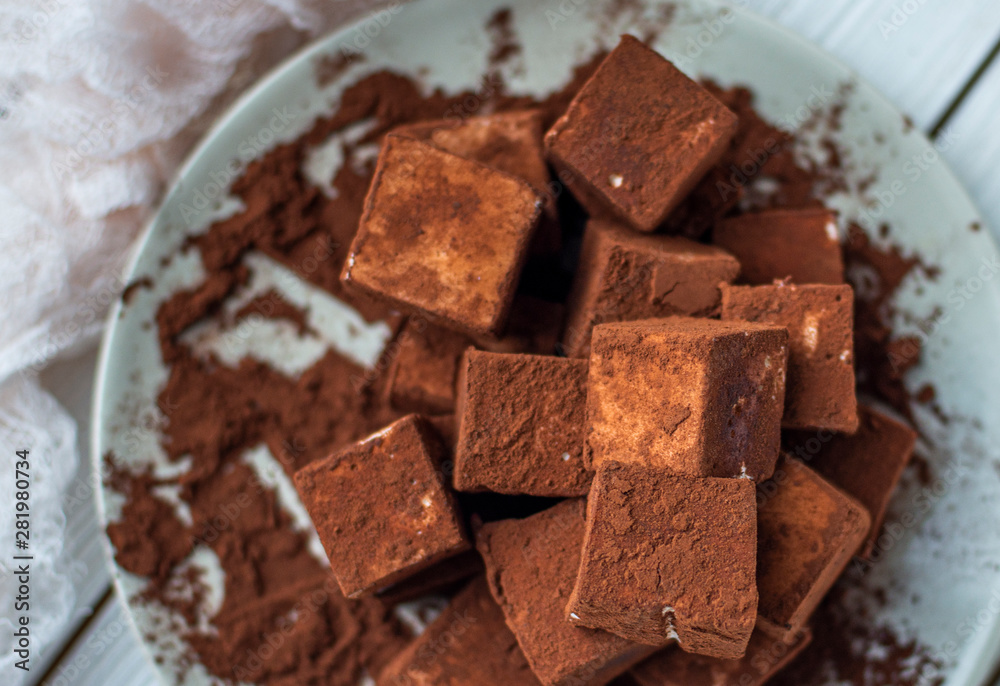 handmade souffle cubes covered with cocoa powder and pieces of chocolate lie on a plate on a light wooden table. handmade souffle cubes covered with cocoa powder and pieces of chocolate lie on a plate on a light wooden table.