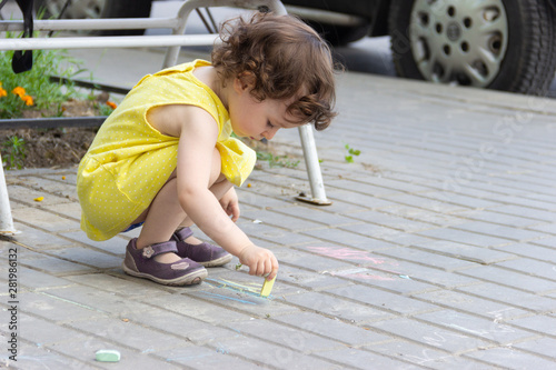 little two three year old girl draws a chalk