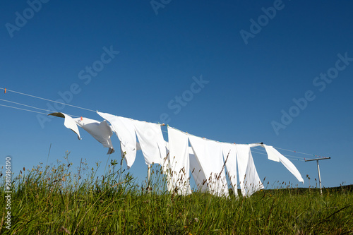 clean white clothes hanging on a rope moved by the wind in green meadow